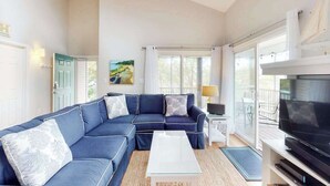 A living room with a sectional sofa, a coffee table, a TV, and a painting on the wall. - Sea Colony Tennis condo with sauna, hot tub & pools - short drive to the beach (Bethany Beach)