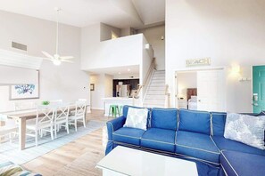 Ein großzügiger Wohnbereich mit einem blauen Sofa, einem Esstisch mit Stühlen, einer Treppe und einer Küche im Hintergrund.