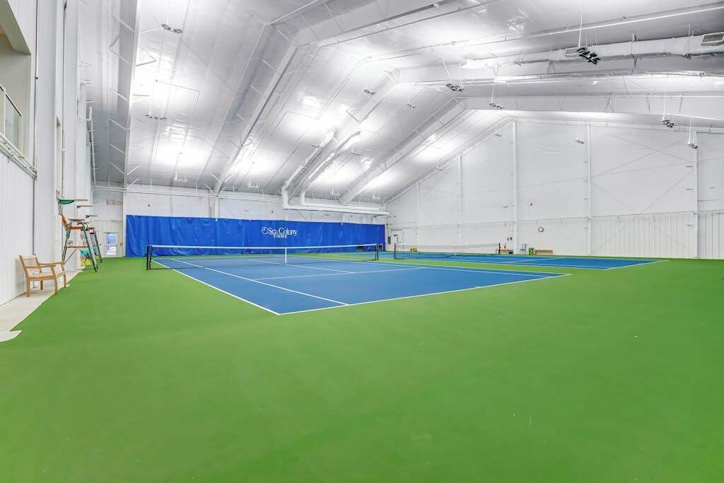 An indoor tennis court with a blue and green floor, white walls, and a blue curtain.