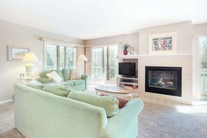 A living room with a sofa, a TV, a fireplace, and a window. - Sea Colony 1st-floor condo with pool, hot tub, sauna, gym, & tennis court (Bethany Beach)