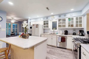 A modern kitchen with white cabinetry, a central island, and a dining area with a table and chairs. - Sea Colony townhome with tennis court, pool, gym, & basketball court (Bethany Beach)
