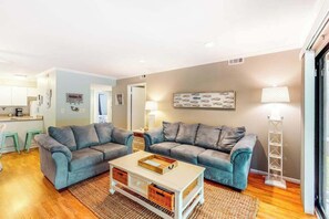 Ein Wohnzimmer mit zwei grauen Sofas, einem Couchtisch und einer Küche im Hintergrund.