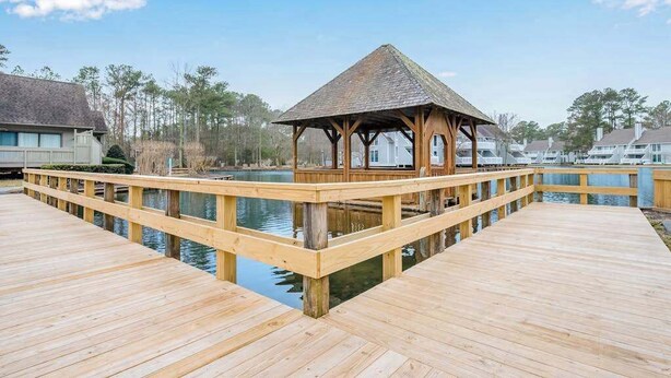Eine Holzterrasse mit einem Pavillon, ruhiges Gewässer und Wohnhäuser im Hintergrund.