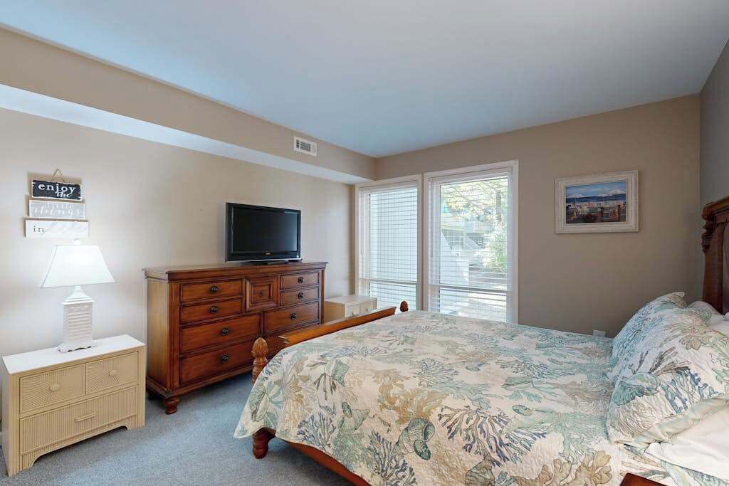 Un dormitorio con cama, cómoda, televisor y ventana con persianas.