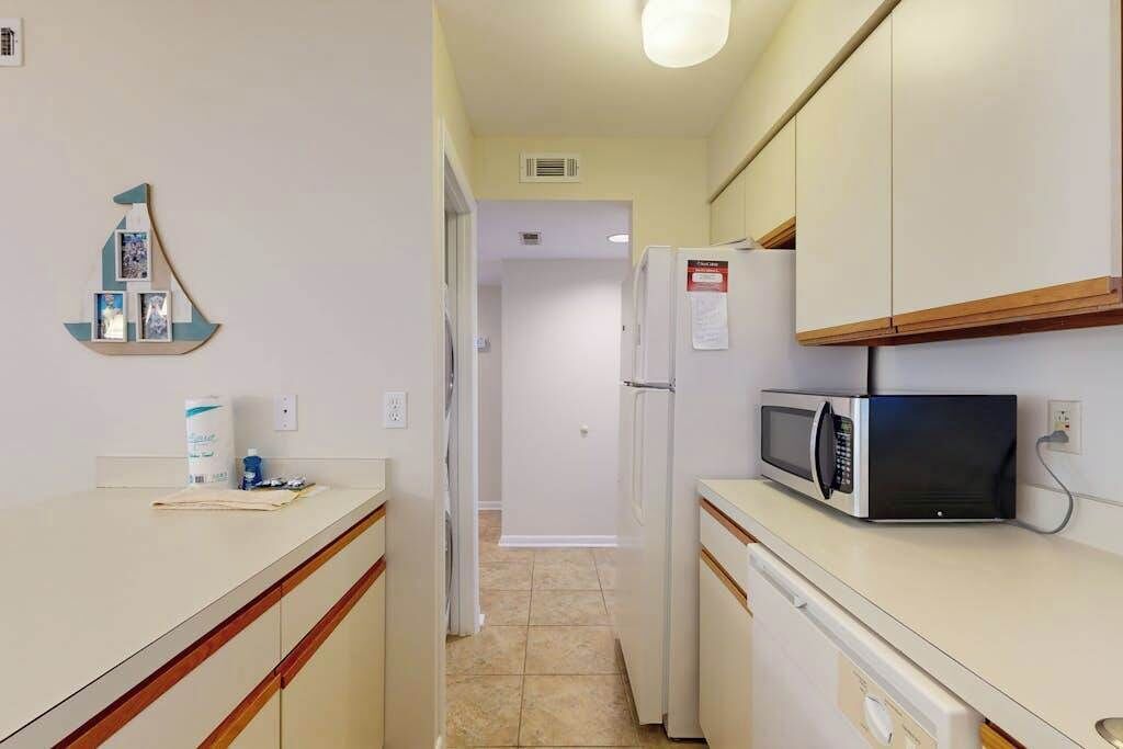 Una cocina compacta con microondas, refrigerador y una pequeña estantería con objetos.