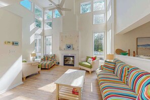 Ein geräumiges Wohnzimmer mit Kamin, großen Fenstern und Deckenventilator.