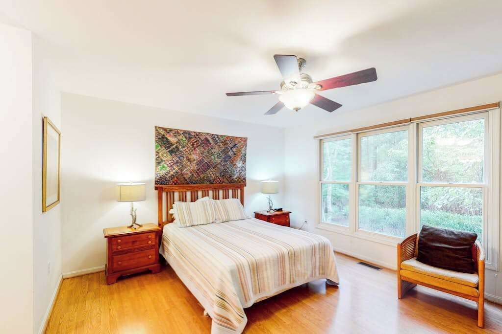 A bedroom with a bed, nightstands, a ceiling fan, a window, and a chair.