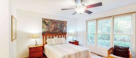 A bedroom with a bed, nightstands, a ceiling fan, a window, and a chair.
