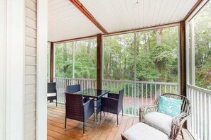 Eine überdachte Veranda mit Korbmöbeln und einem Glastisch, mit Blick auf ein bewaldetes Gebiet.