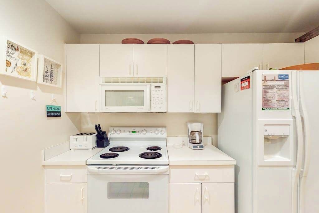 A compact kitchen with white cabinets, a microwave, a stove, and a refrigerator.