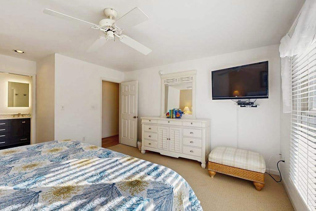 A bedroom with a bed, a dresser, a television, and a ceiling fan.