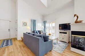 Un salon avec un canapé gris, un téléviseur, une cheminée et une fenêtre avec des rideaux.