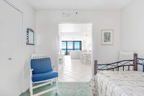 A bedroom with a bed, a blue chair, a white radiator, and a view of the sea through a large window. - Sea Colony Ocean 3rd floor condo w/ shared sauna, elevator, and gym (Bethany Beach)