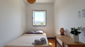 A bedroom with a single bed, a window with an open view, a wooden bedside table with a plant, and a hanging light fixture. - Santos (Lisbon)