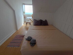 Una habitación pequeña con cama individual, suelo de madera, alfombra a rayas colorida y un par de toallas dobladas sobre la cama.