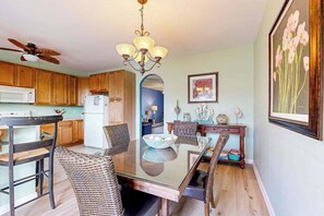 A dining area with a glass table, wicker chairs, a ceiling fan, a white refrigerator, wooden cabinets, and a framed floral artwork on the wall. - Bayside Resort townhouse with private gas grill and golf on-site (Selbyville)