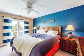A bedroom with a bed, two bedside lamps, a ceiling fan, a wooden headboard, and a window with curtains. - Bayside Resort townhouse with private gas grill and golf on-site (Selbyville)