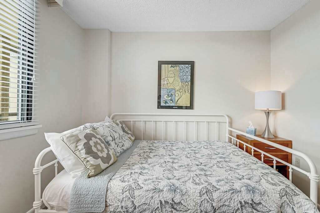 Une chambre à coucher avec un lit, une table de chevet, une lampe et un tableau accroché au mur.