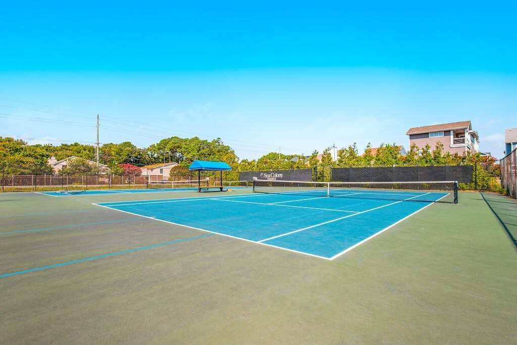 A tennis court with a net, surrounded by a fence, and a building in the background.