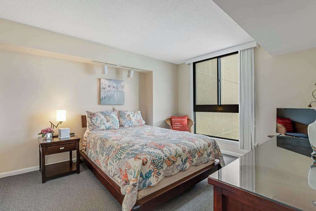 A bedroom with a bed, a nightstand, a lamp, a painting on the wall, and a window.