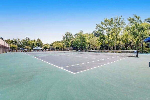 Un campo da tennis con una rete, circondato da alberi e un edificio.