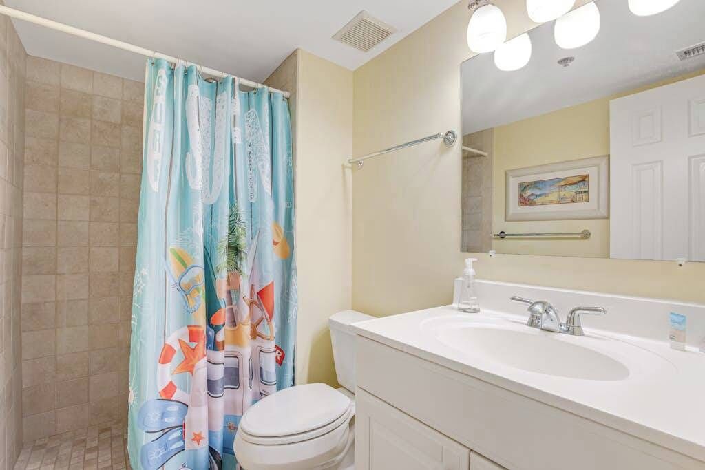A bathroom with a shower curtain, toilet, sink, and mirror.