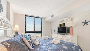 Ein Schlafzimmer mit einem Bett, einem Fernseher, einem Schminktisch und einem Fenster mit Jalousien.