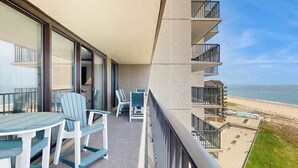 A balcony with a view of the beach, a table with chairs, and a pool area. - Sea Colony Ocean 9th floor condo w/ elevator, tennis court, and pool (Bethany Beach)