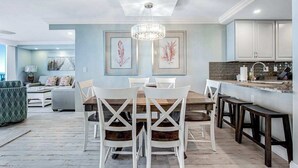 Un coin repas avec une table en bois, des chaises blanches et un lustre.
