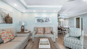 Un salon comprenant un canapé, un fauteuil, une table basse et des œuvres d’art accrochées au mur.