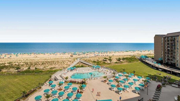 Un hôtel doté d’une piscine, offrant une vue sur la plage, et dont le bâtiment principal est situé sur la droite.