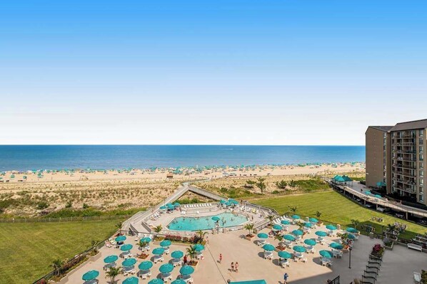 Een hotel met een zwembad, uitzicht op het strand en een groot gebouw aan de rechterkant.