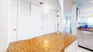 Een keuken met een granieten aanrecht, witte kastjes en uitzicht op de woonkamer.