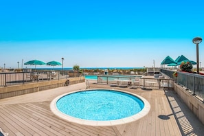Zona de piscina amb terrassa de fusta, gandules i ombrel·les.