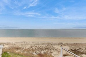 Ein Strand mit blauem Himmel, sandigem Ufer und einem Gebäude mit einem Weg zum Wasser.