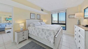 Un dormitorio con cama, mesitas de noche, cómoda, ventana con vistas y televisor.