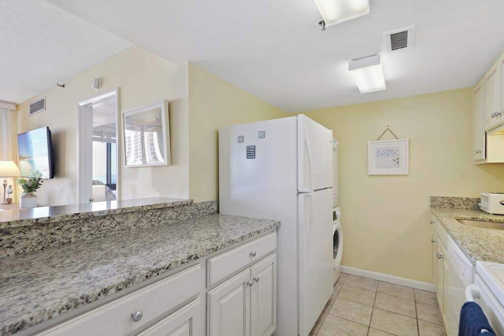 A compact kitchen with white cabinets, a granite countertop, a white refrigerator, and a small sink.
