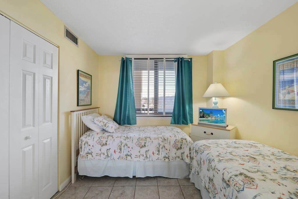 Un dormitorio con dos camas, una ventana con cortinas, una lámpara de noche y un cuadro en la pared.