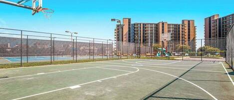 Una cancha de baloncesto al aire libre con aro, rodeada por una cerca de malla metálica.