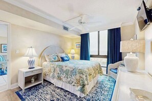 Ett hotellrum med en säng, två sängbord, en stol, en tv och ett stort fönster.
