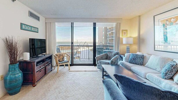 A living room with a television, sofa, and a large window with a view of the beach. - Sea Colony Ocean 2nd floor condo w/ pool, basketball court, and free WiFi (Bethany Beach)