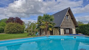 Ein Pool mit einem Holzhaus im Hintergrund, umgeben von viel Grün.