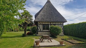 Ein traditionelles Reetdachhaus mit Steinunterbau, umgeben von einem gepflegten Garten und einem Heckenstreifen.