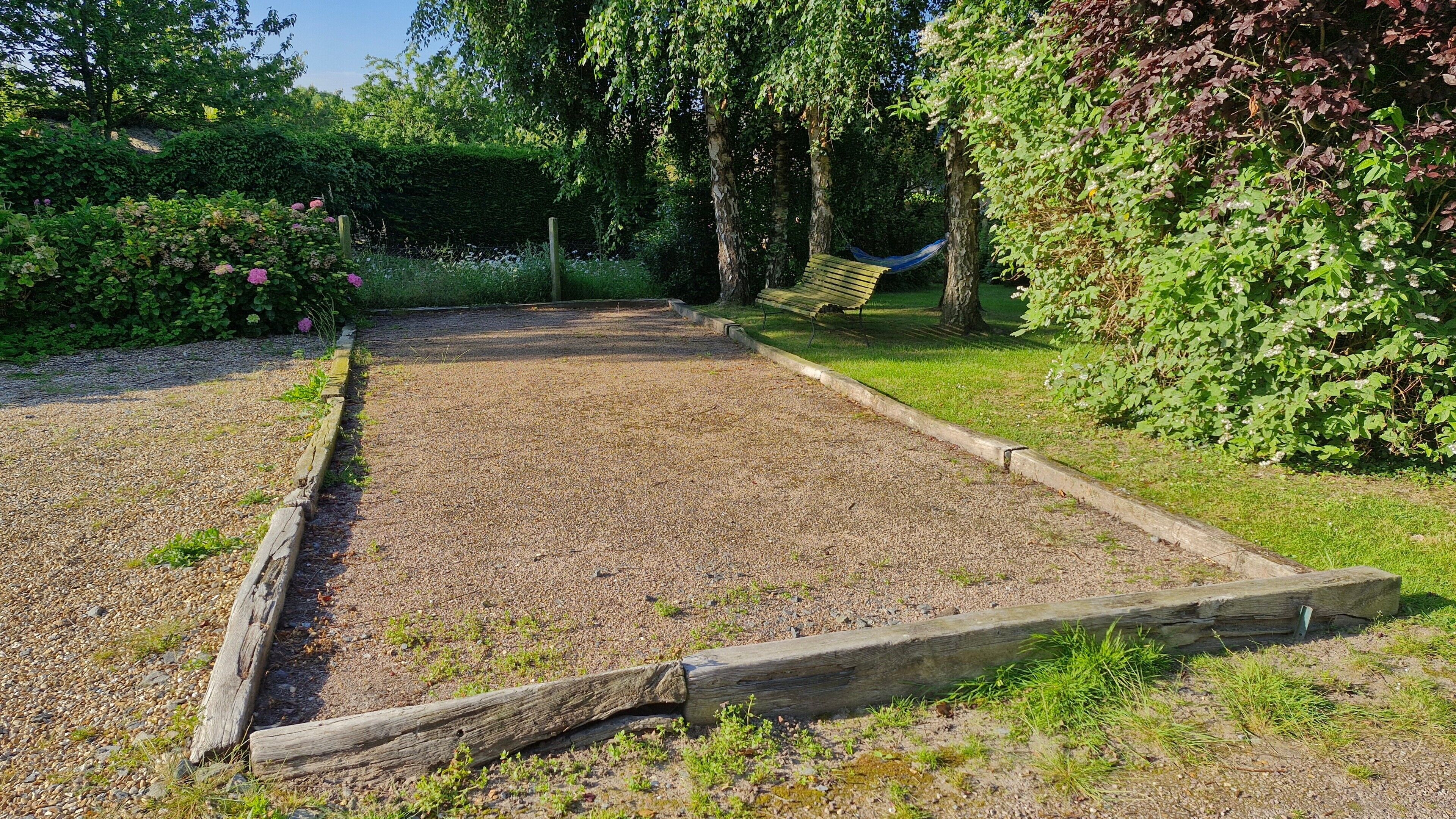 A garden with a raised garden bed, a hammock, and a wooden bench.