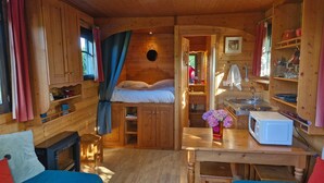 A cozy cabin interior with a bed, wooden walls, a small kitchen, and a dining area. - Bohemian Caravan Cottage for 2–4 Guests near Honfleur with Pool (Fatouville-Grestain)