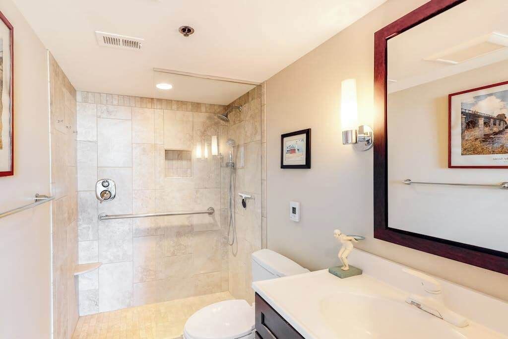 A bathroom with a shower, toilet, sink, and a large mirror.