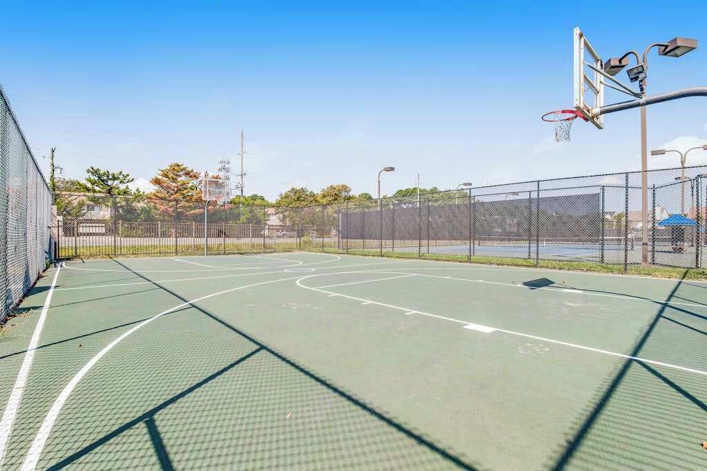 Ein Basketballplatz im Freien mit Netz, umgeben von einem Maschendrahtzaun und blauem Himmel im Hintergrund.