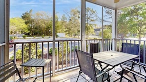 A covered outdoor area with a table and chairs, large windows, and a view of a street and trees. - Sea Colony Tennis 1st-floor condo with gym, tennis court & private beach (Bethany Beach)