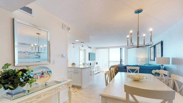 Una cocina moderna con muebles blancos, un comedor con mesa y sillas blancas, y un amplio ventanal que proporciona luz natural.