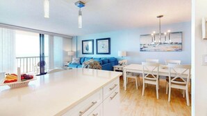 Una cocina moderna con una isla central, un comedor con sillas blancas y un sofá azul.